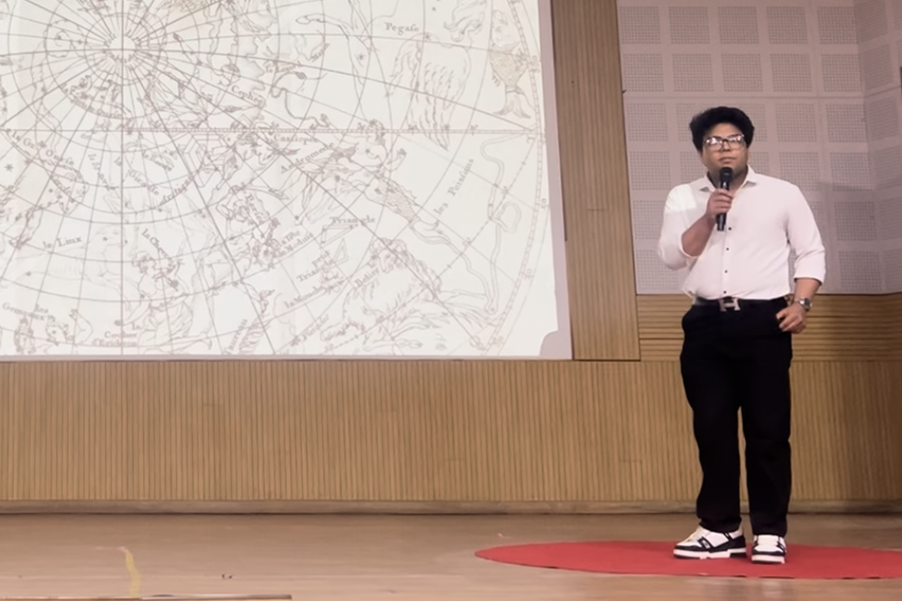 Candid photo of a teenager standing on a stage speaking into a microphone next to a world map.