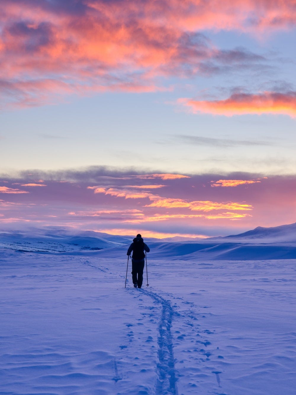A woman trying to walk in the snow with hiking poles during sunset.