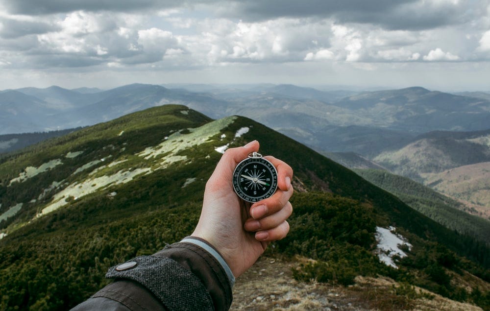 A man holding a compass in the middle of mountains