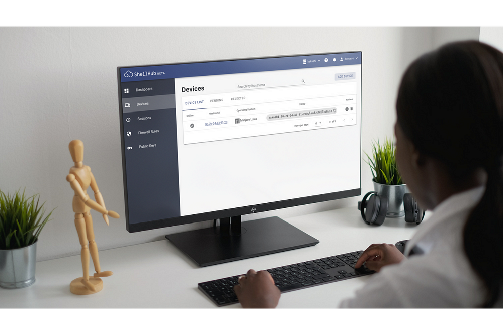 mulher jovem em frente a um monitor onde utiliza o shellhub para visualizar sua lista de dispositivos e acessá-los remotamente