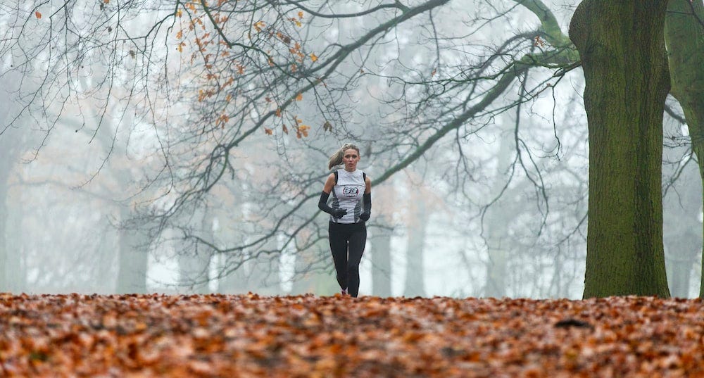 A woman is running under bare trees in the forest. Fil Mazzarino/Unsplash.