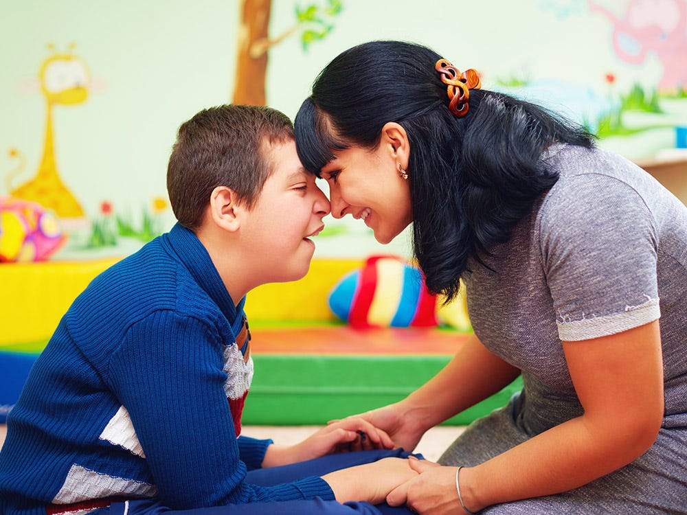 A women showing her love towards a autistic child by holding his hands and touching his nose by her nose