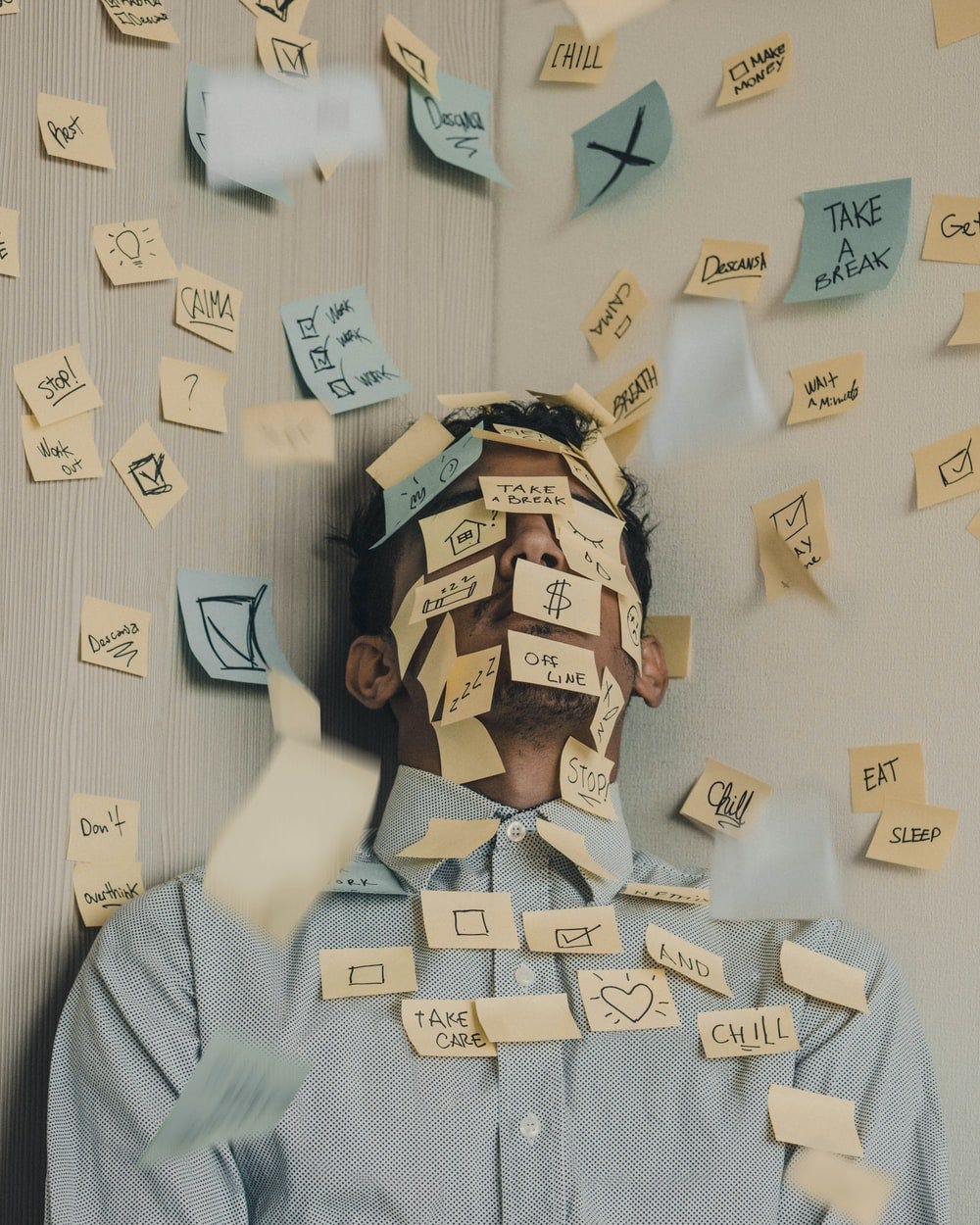 A man’s face and area around it covered with blue and yellow sticky notes on which words and symbols related to tiredness are mentioned.