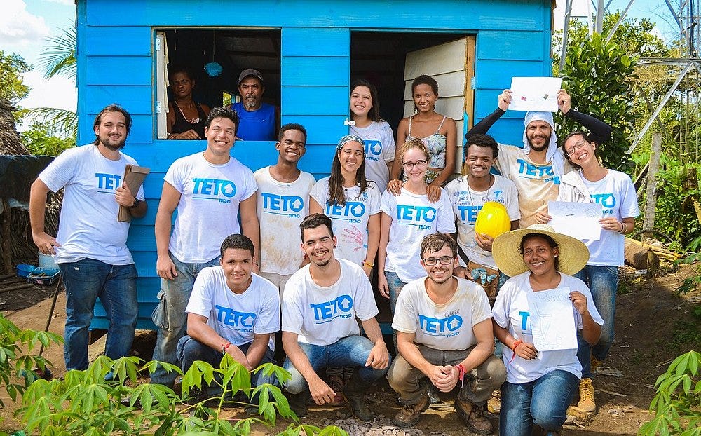 Grupo de voluntários da TETO reunídos em frente a uma casa, sorrindo para a foto