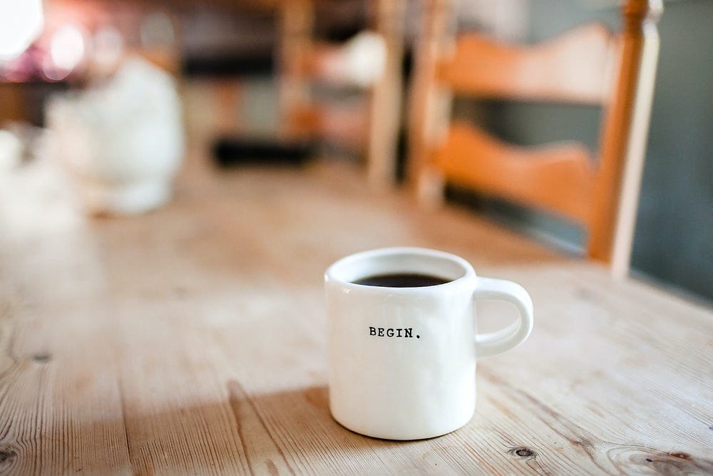 White ceramic mug on table with words “Begin” written on the mug