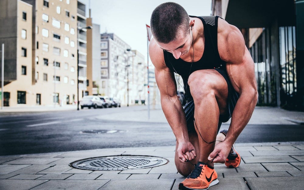 A fit man is tying his shoelaces in the street. Alexander Redl/Unsplash.