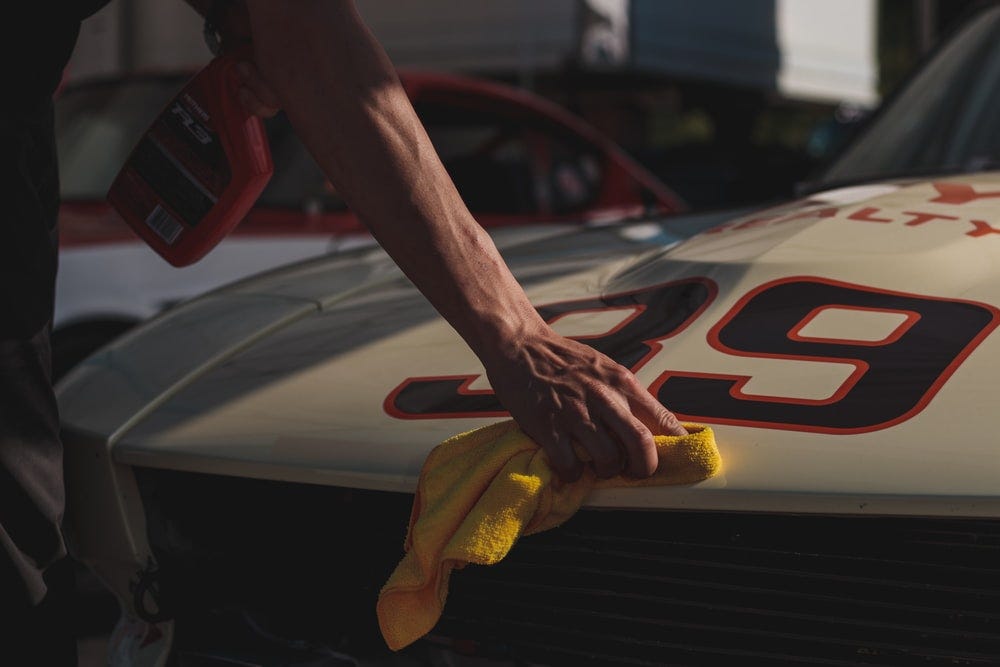 A man wiping the surface of a nice sports car.
