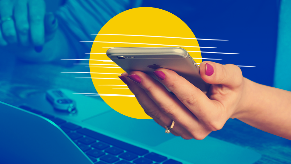 Woman’s hand holding silver iphone in front of yellow circle, with laptop in blue background