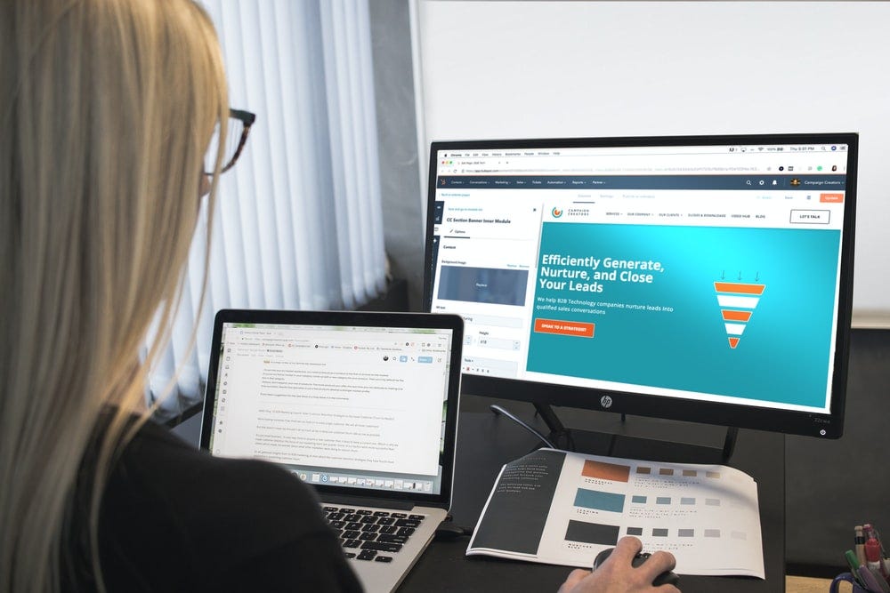 A woman is sitting in front of a PC and a laptop while designing a website. Image by Campaign Creators on Unsplash.