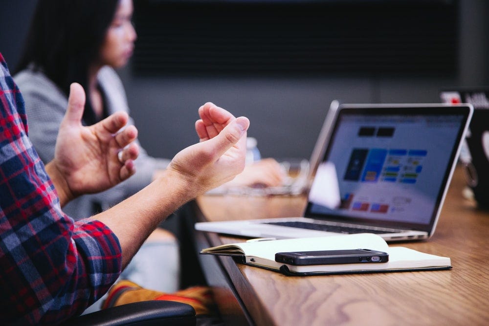 A male gesturing his hands when talking  with others in the room trying to have a conversation.