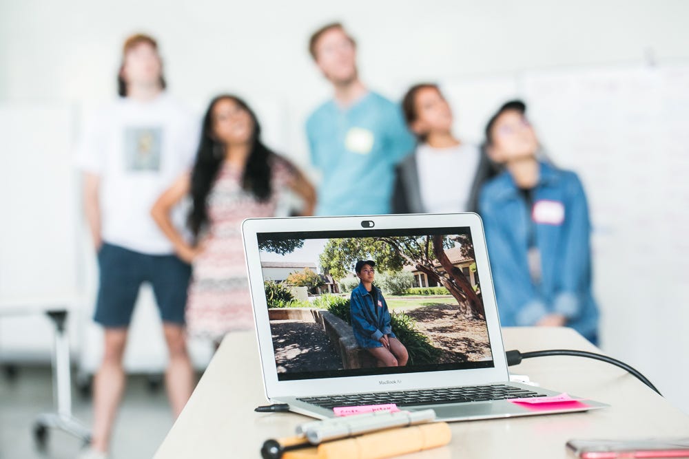 Close up of a laptop with a photo of a girl, in the background of the photo five students are looking upwards.