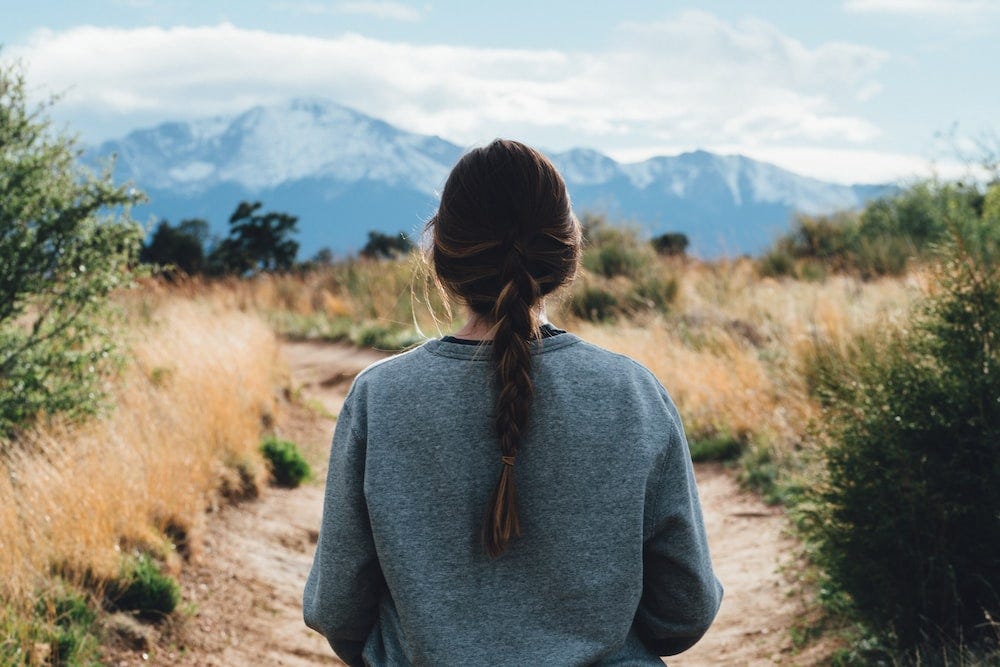 A woman is walking through a pathway in a field during the daytime. Alexander Ramsey/Unsplash.