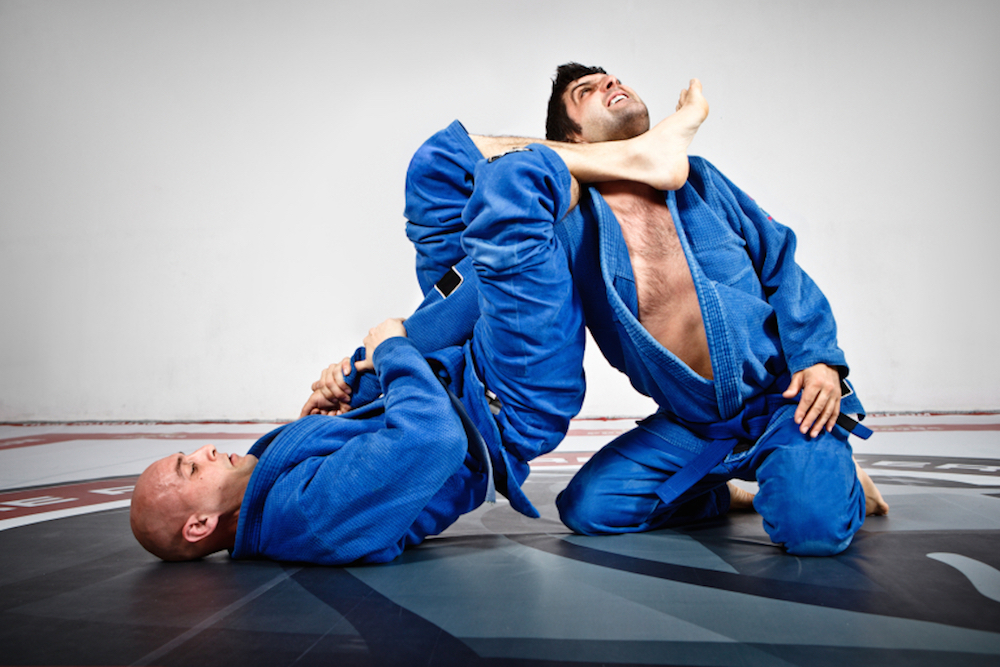 A man uses Brazilian Jiu-Jitsu and holds his opponent in an ankle choke-hold