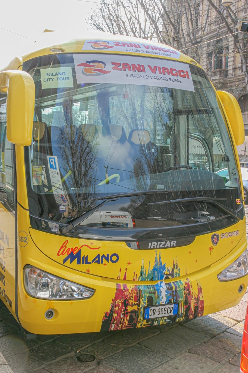 The front of a bright yellow Zani Viaggi tour bus with a large windshield. The interior of the bus is blurry because of glare.