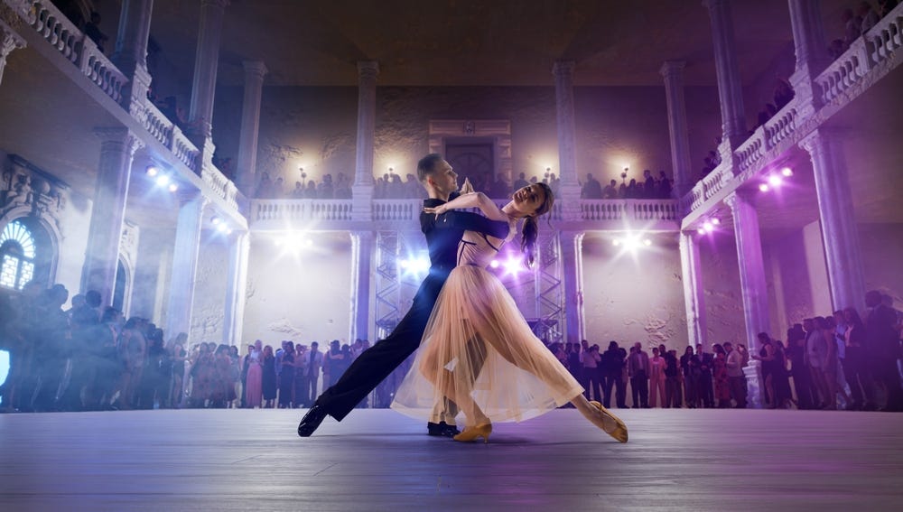 A man and a lady doing a waltz dance in purple light