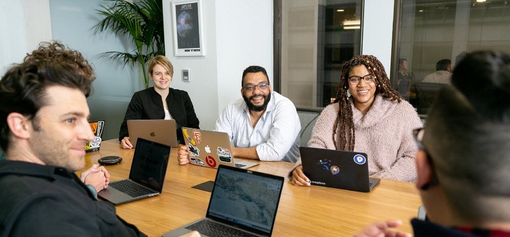 diverse team around table with computers looking happy