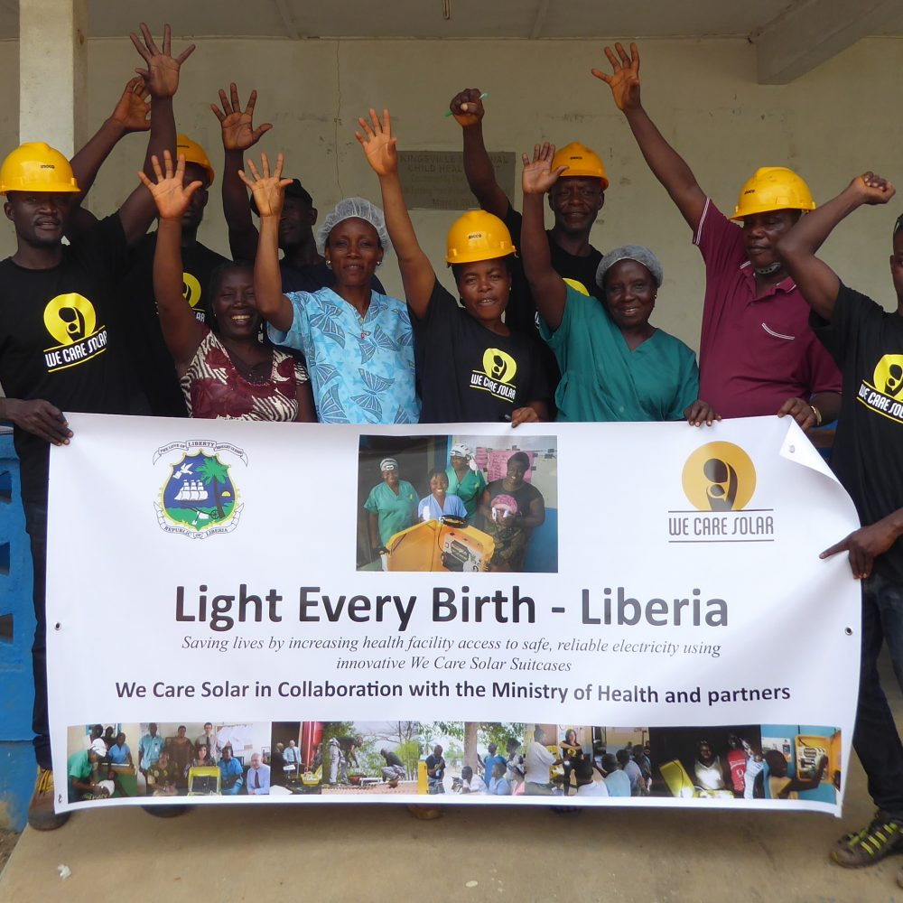 Group of people holding wearing hard hats holding a sign that says “Light Every Birth — Liberia”