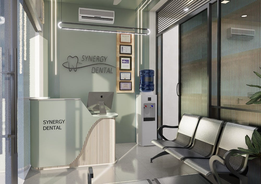 A modern dental clinic interior design featuring a soft green reception area at Synergy Dental. The space includes a sleek curved desk with a computer, framed certificates, and a water dispenser. Black metal seating provides patient-friendly comfort, while glass partitions bring in natural light. Clean lines, soothing colours, and functional layout create a professional and welcoming dental clinic reception design.