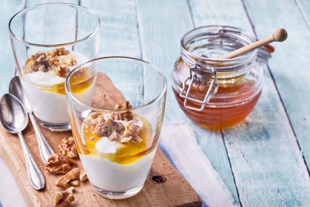 Two glasses of Greek yogurt topped with honey and walnuts.