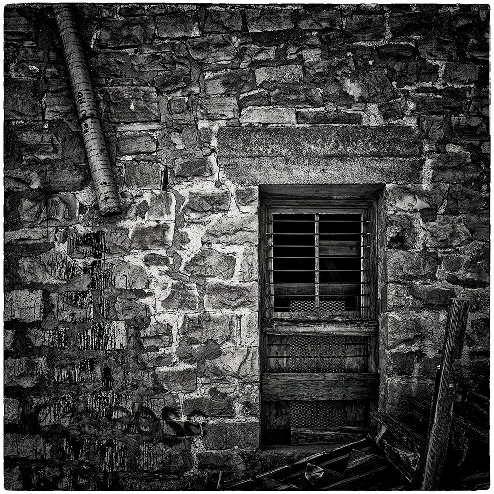 Black and white image of a stone wall and wooden door of an abandoned motel and general store in Duran, New Mexico