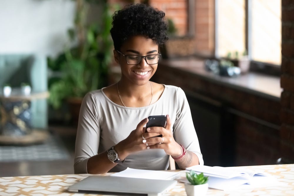 A lady smiling while using her phone indicating she is having a nice time.