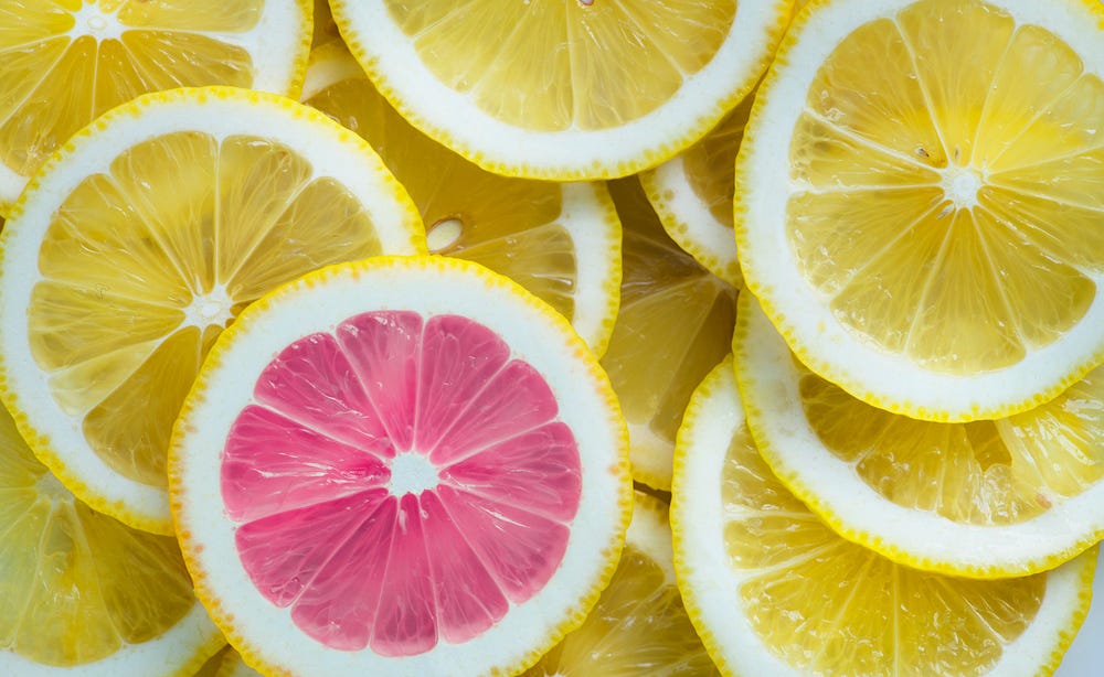 Slices of yellow lemon, pictured from above. On pink lemon standing out from the crowd.