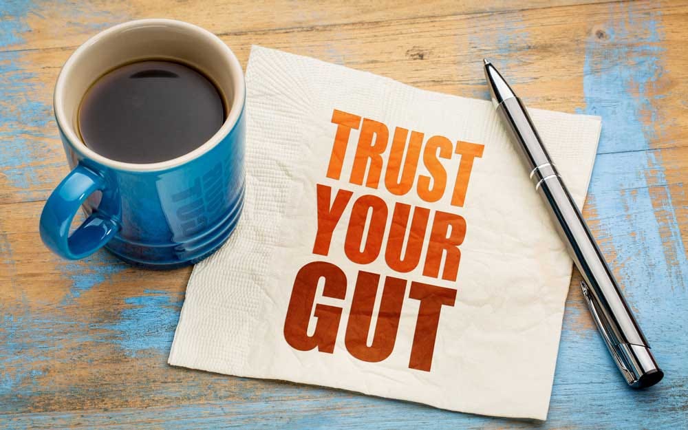 Napkin with “trust your gut” on it under a cup of coffee and a pen