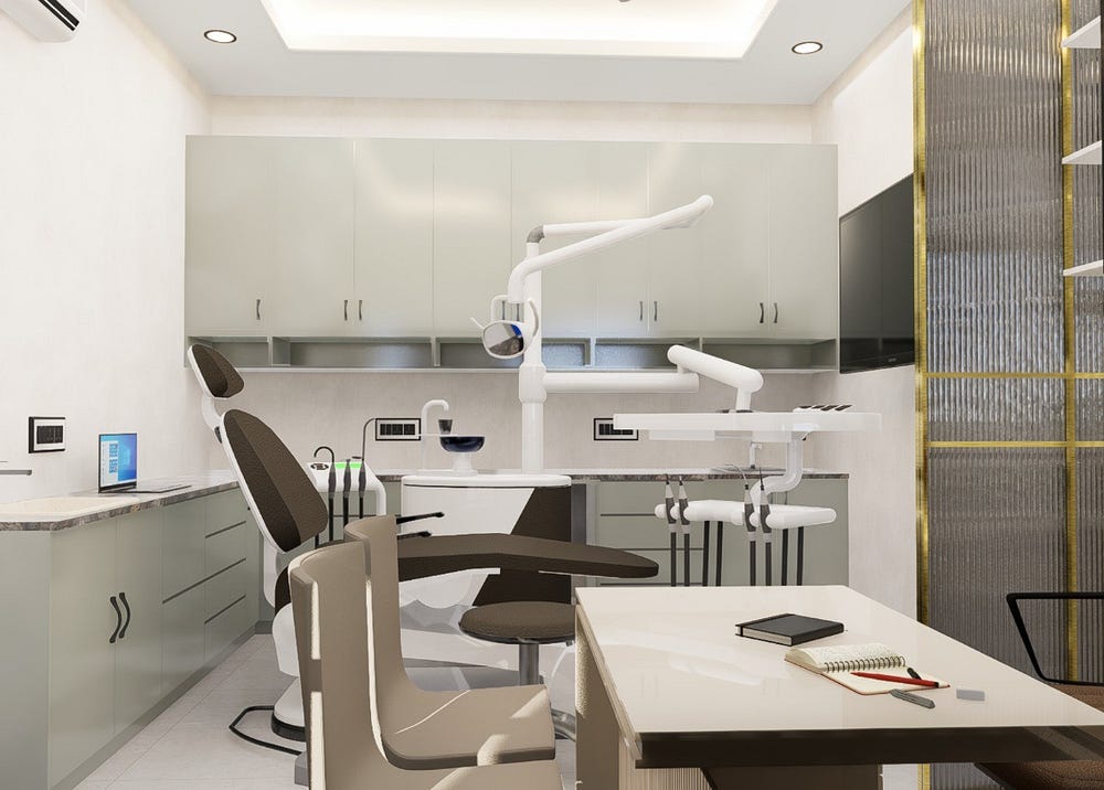 A clean and modern dental treatment room featuring a reclining dental chair with attached equipment, overhead examination light, and organized cabinetry for instruments. A desk with notebooks and seating for consultation is placed nearby. Light-coloured walls and cabinetry, along with a mounted TV and glass partition, create a professional yet calming environment that ensures patient comfort and hygienic dental care.