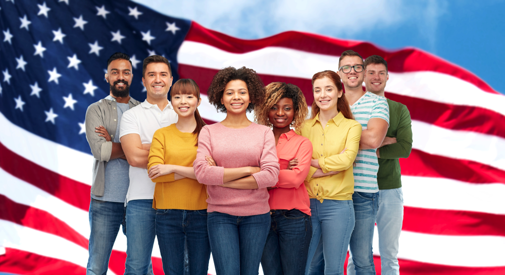 Eight people from diverse backgrounds stand with arms crossed in front of an American flag.