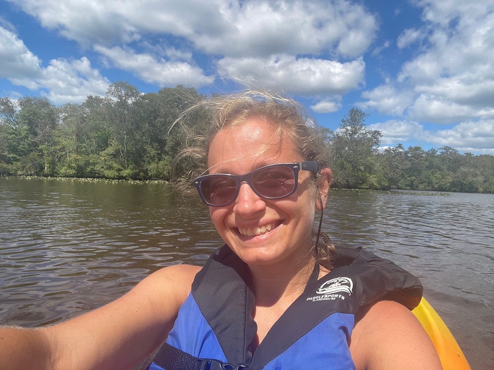 Me smiling in a kayak on a river with trees behind me.