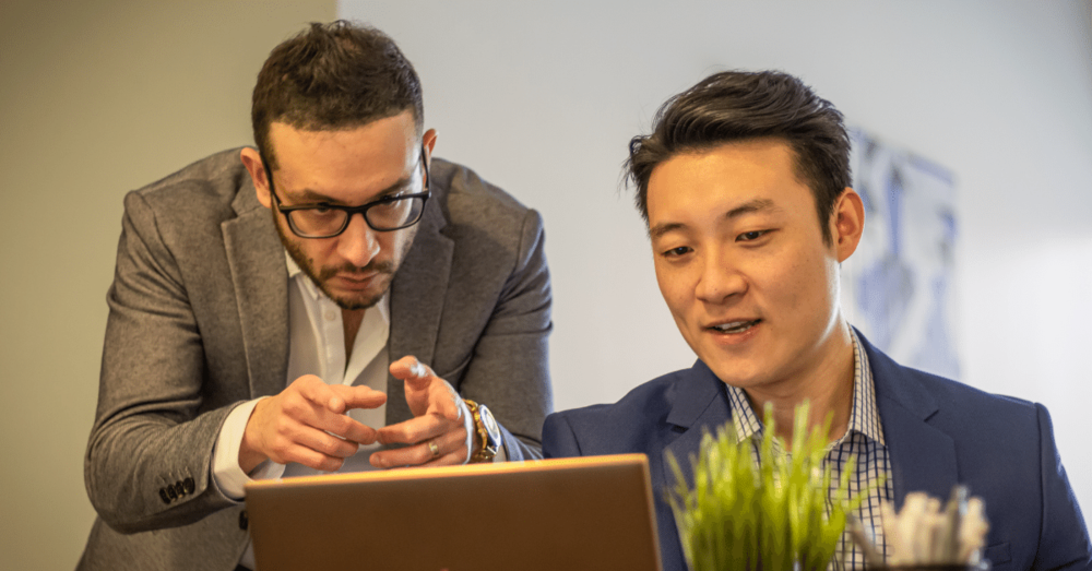 two men working together at a computer discussing options