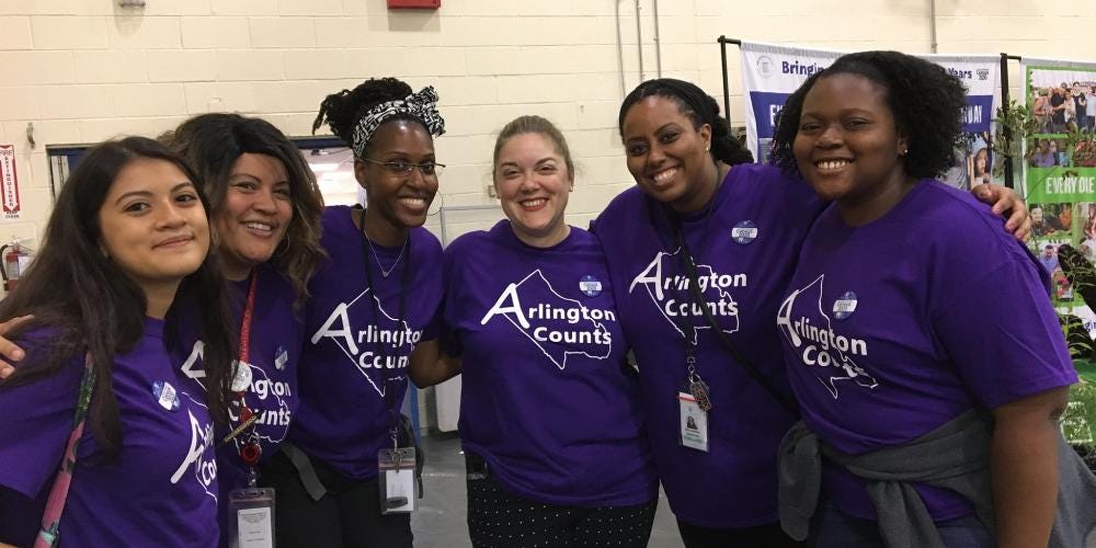 Five women wearing purple t-shirts that read “Arlington Counts” stand arm-in-arm.