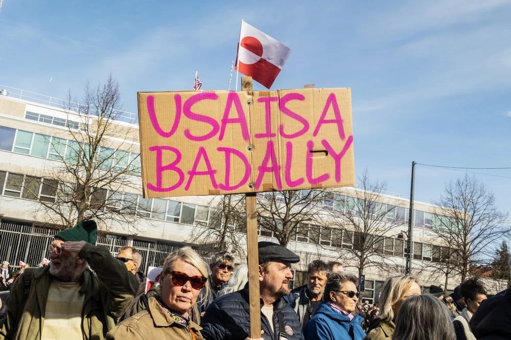 After Trump declares his interest in taking over Greenland, protests erupt in Denmark. This is a photo of a protest rally in which a protester is holding up a sign that says, in English, “USA IS A BAD ALLY”.