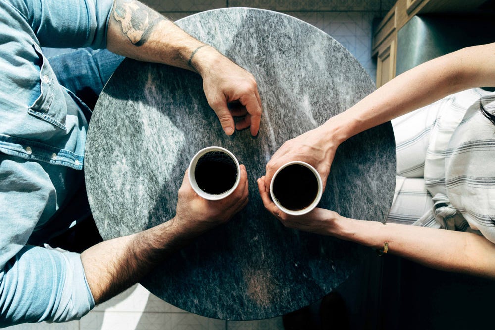 Photo taken from above of two people talking and drinking coffee
