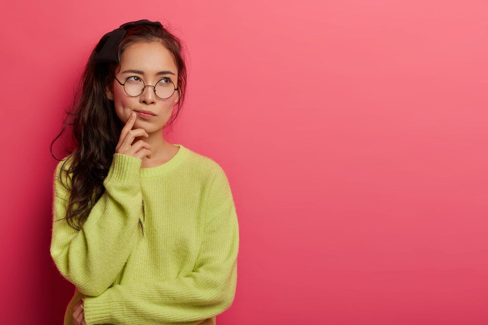 a woman in a green cardigan deep in thought with a finger on her cheek