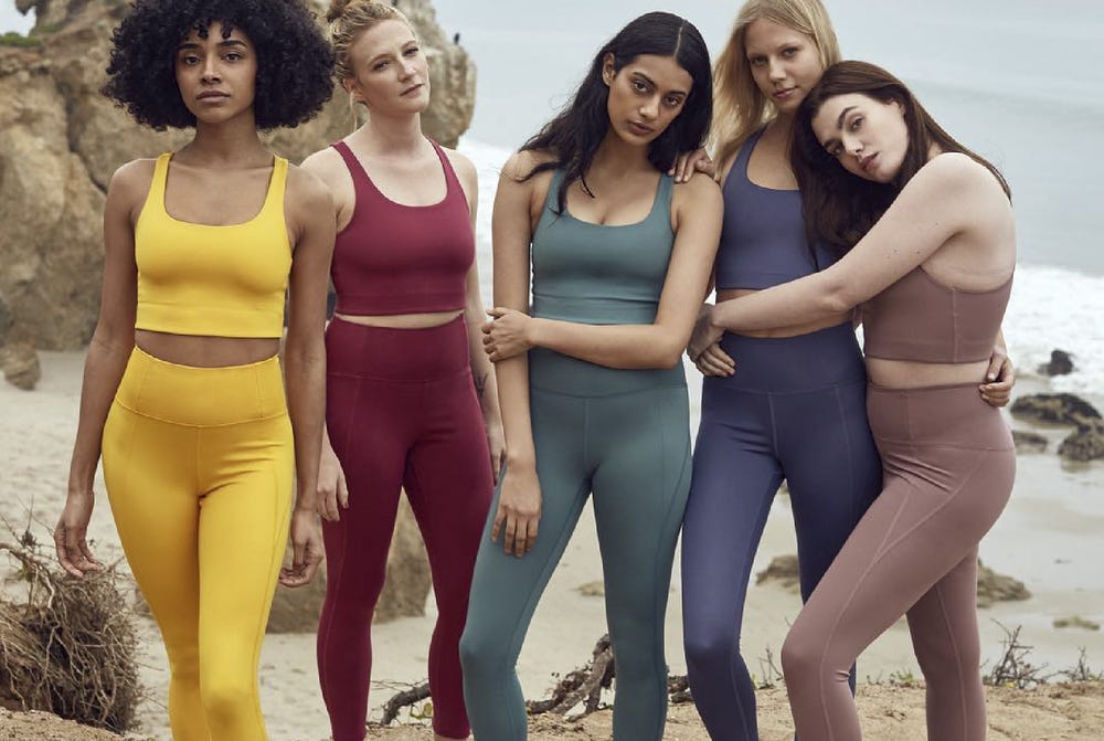 A group of five women on a beach wearing colourful and sustainable sportwear.