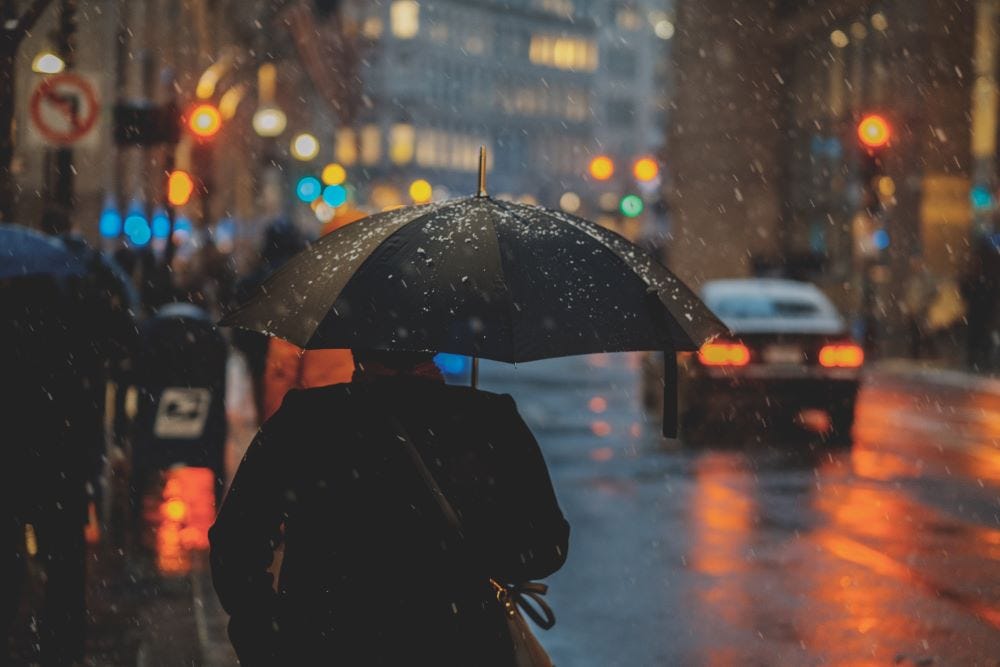 A man with a black umbrella walking through a rainy downtown district