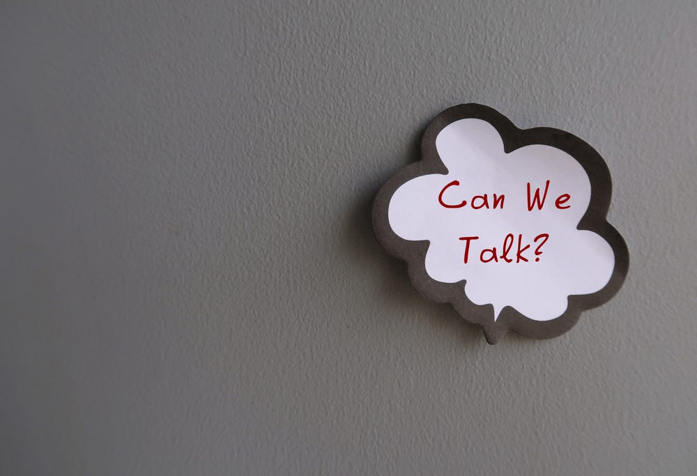 A wall with a sticker on it, saying “Can we talk?”