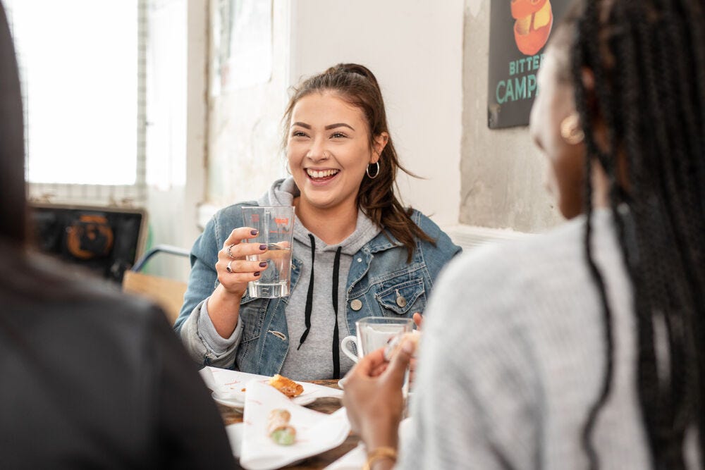 A student is smiling while speaking to friends — they are eating and drinking.
