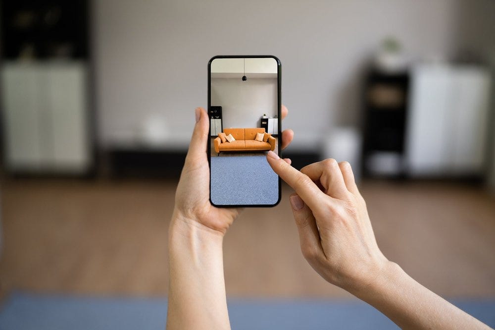 A woman is holding up her smartphone as an augmented reality device. The smartphone overlays a dimensionally accurate virtual sofa in an empty space. AR has the potential for retail applications and virtual environment building.