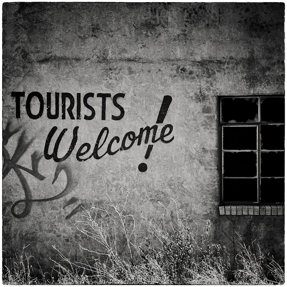 Black and white image of an adobe facade painted with the words Tourists Welcome!