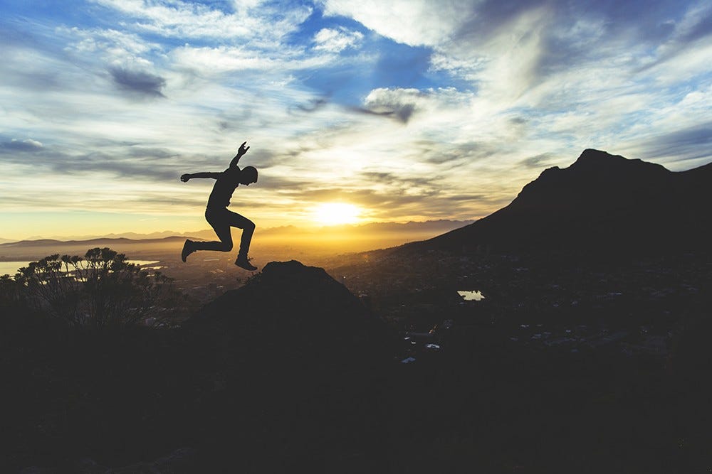man jumping with mountains and sunrise as the background