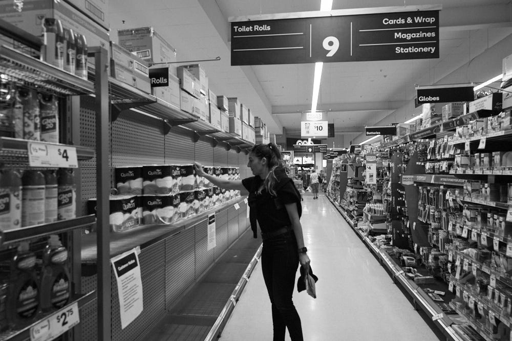 A person standing in front of almost empty tiolet paper shelf in store