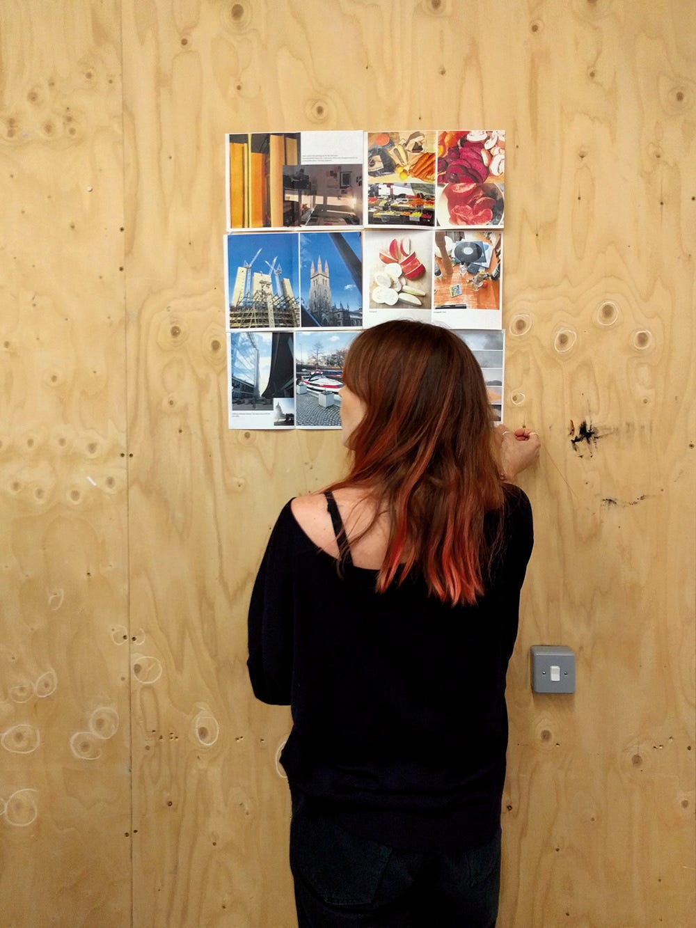 A woman standing in front of a wooden office wall looking at printed photographs of public infrastructure
