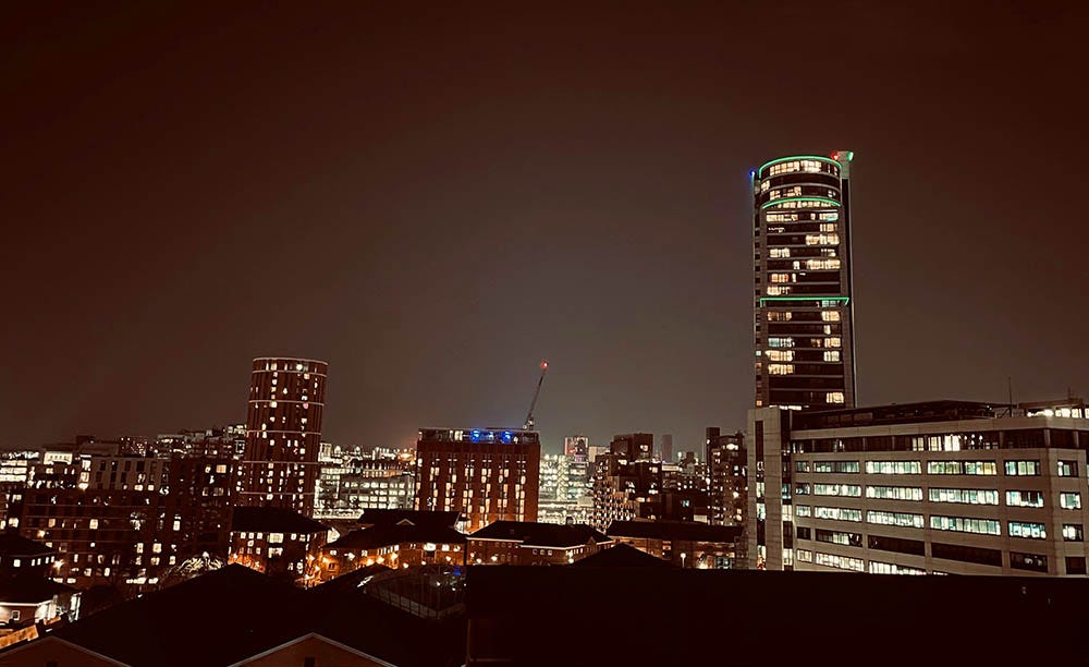 A wide angle panorama of Leeds City Centre at night, detailing high-rise buildings with glowing windows.
