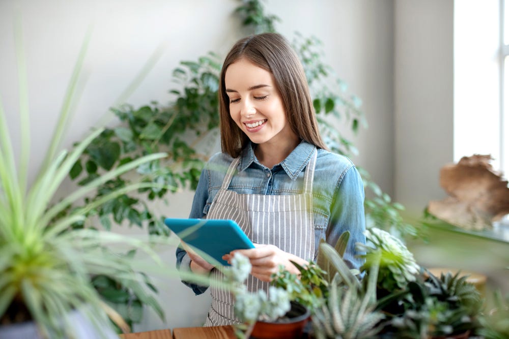 Mujer rodeada de plantas y mirando sonriente una pantalla porque ha conectado con los valores de su proveedor.