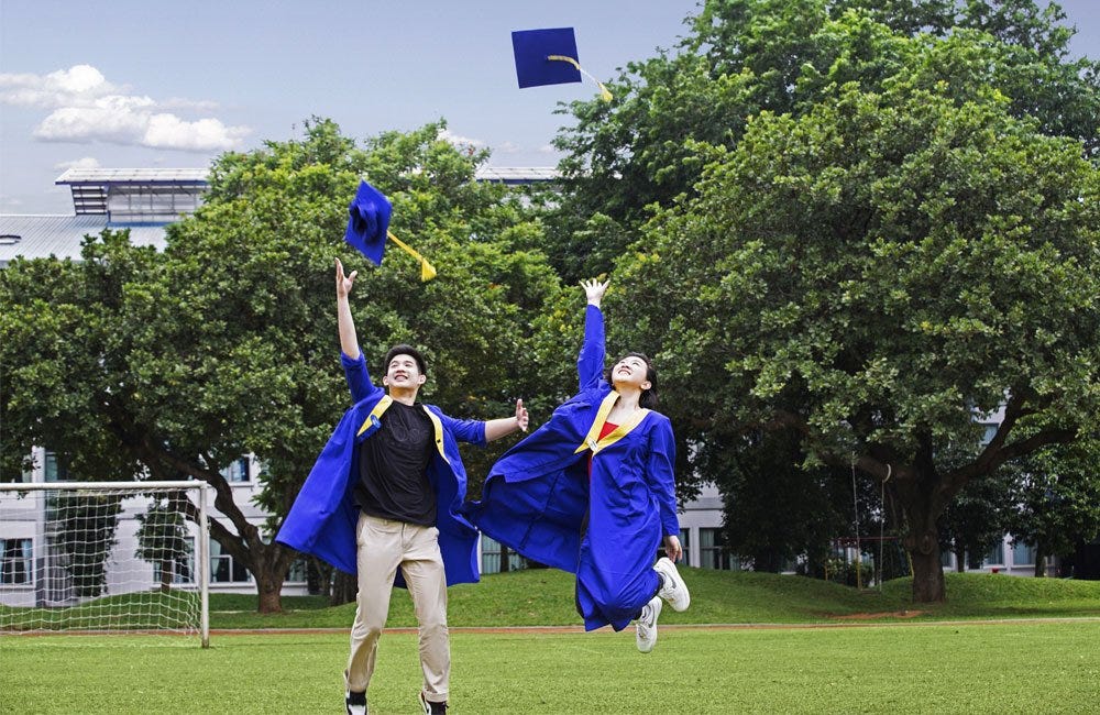 Two German School Jakarta graduates jump into the air at the school campus football field