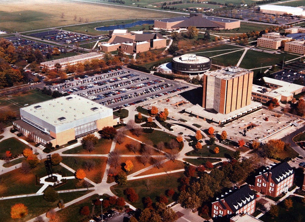Aerial view of Bowling Green State University which includes Carillon Park (which I don’t believe was called that when I went to school there) in the foreground, with its array of sidewalks, Anderson Arena (now Memorial Hall) , Jerome Library, Saddlemire Student Services Building (a disc-shaped building), Moore Musical Arts Center, the Student Recreation Center, and part of the Kreischer Quadrangle (student housing).