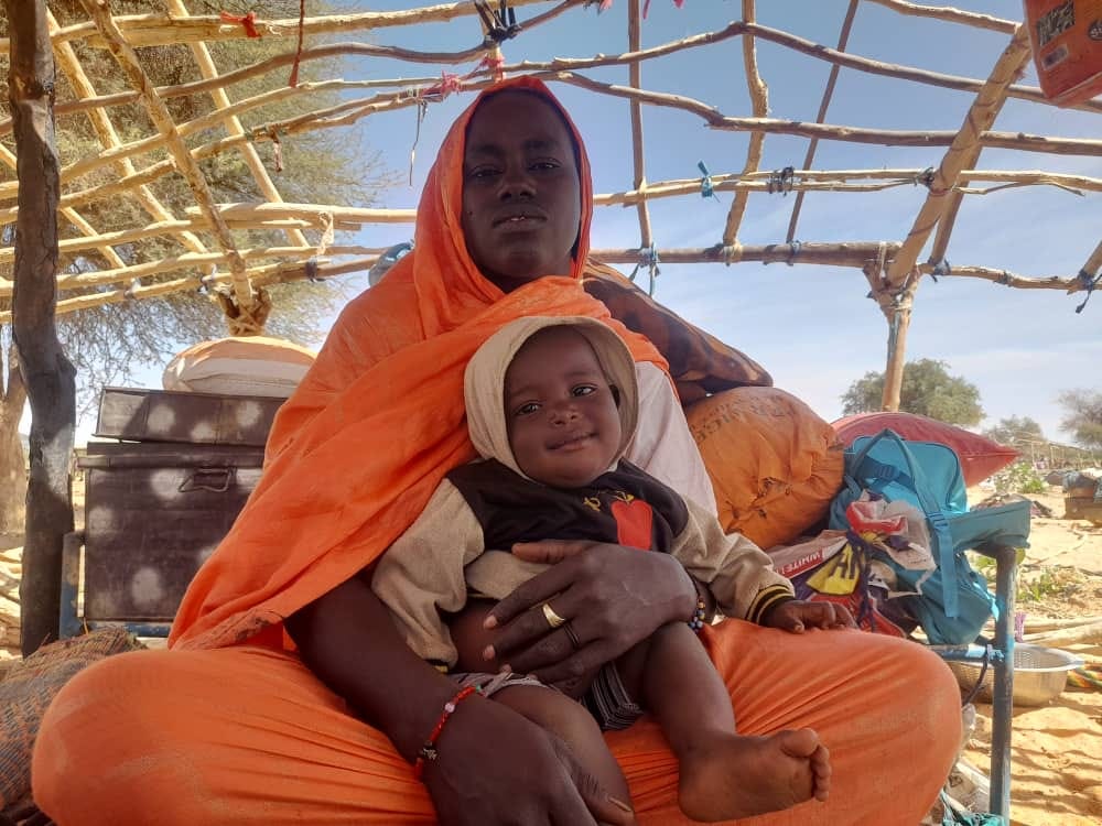 Adiza* mère de famille déplacée, assise avec son enfant sous un hangar.. Photo : PAM/ Aboubacar Sidibé