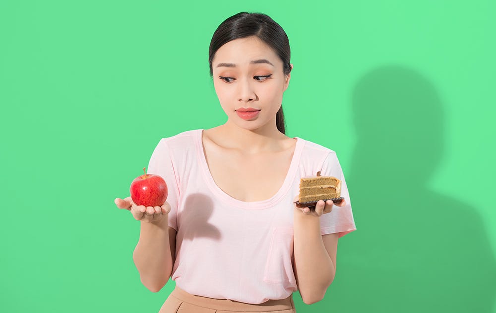 A woman thinks about the choice to either eat an apple or a cake